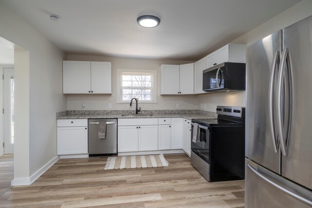 kitchen with light stone countertops, a sink, appliances with stainless steel finishes, white cabinetry, and light wood-type flooring