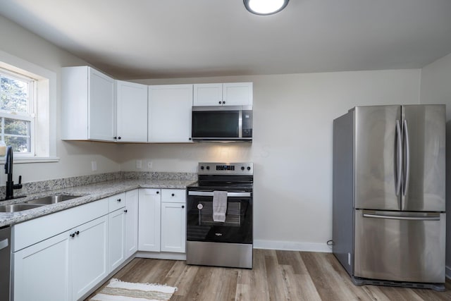 kitchen featuring white cabinetry, light stone countertops, appliances with stainless steel finishes, and a sink