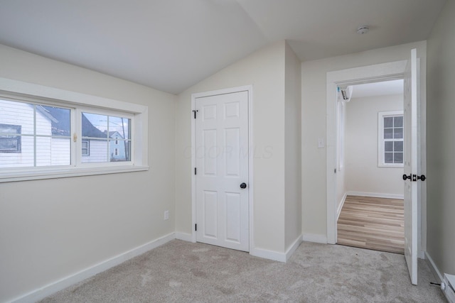 unfurnished bedroom featuring light colored carpet, baseboards, and vaulted ceiling