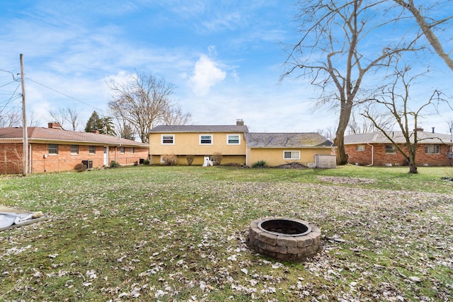 rear view of property featuring an outdoor fire pit, a lawn, a chimney, and stucco siding