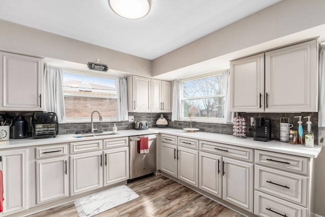 kitchen with tasteful backsplash, light countertops, dishwasher, and a sink