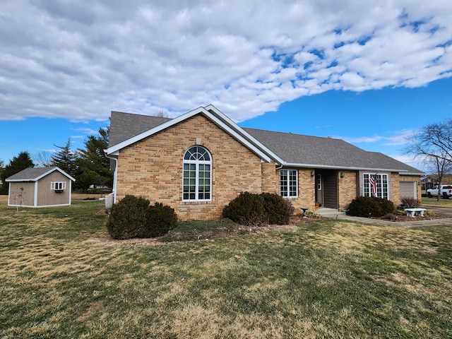 single story home featuring a front yard, brick siding, an outdoor structure, and roof with shingles