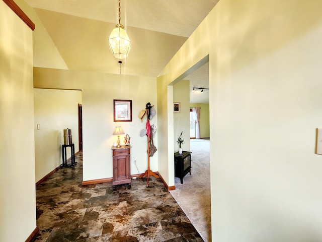 hall with track lighting, dark carpet, stone finish floor, and baseboards