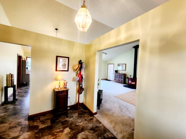 hallway with lofted ceiling, baseboards, and dark colored carpet