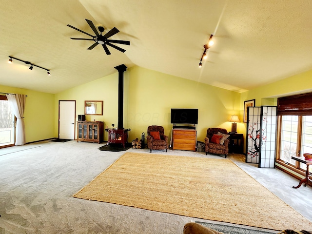 interior space with a textured ceiling, carpet floors, a wood stove, vaulted ceiling, and rail lighting