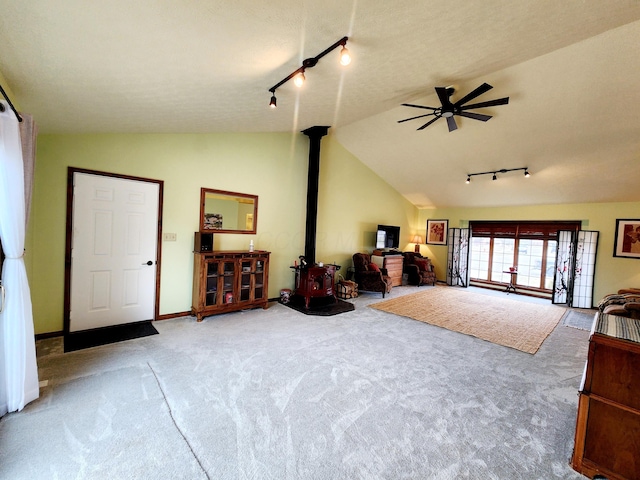 interior space with ceiling fan, baseboards, vaulted ceiling, a wood stove, and track lighting