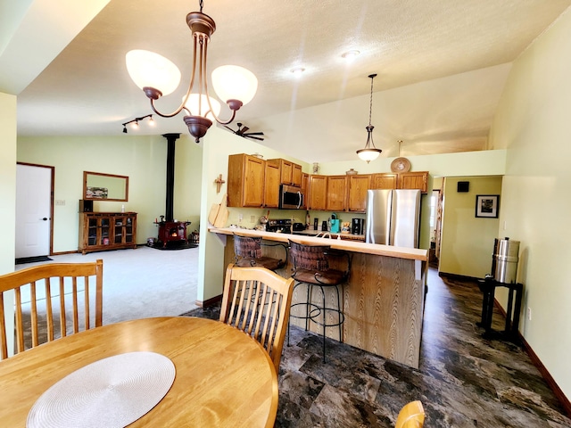 dining room featuring baseboards, a wood stove, vaulted ceiling, dark colored carpet, and a chandelier