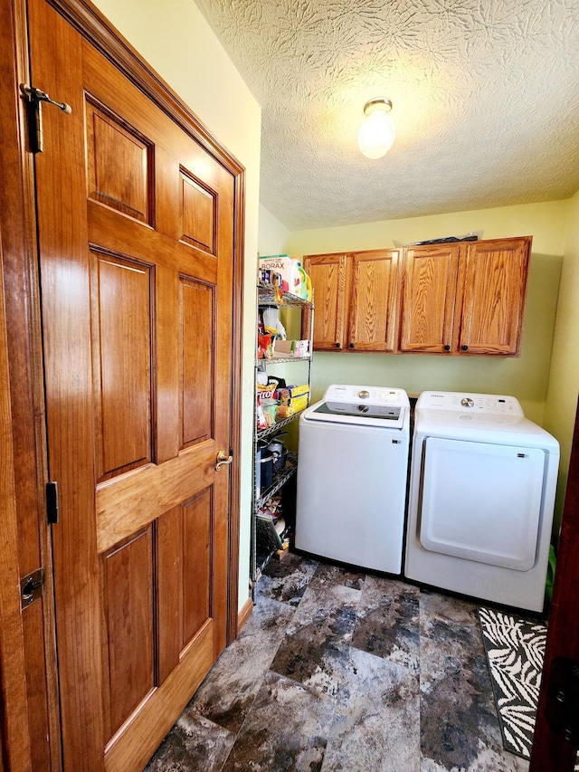 clothes washing area featuring a textured ceiling, washing machine and clothes dryer, and cabinet space