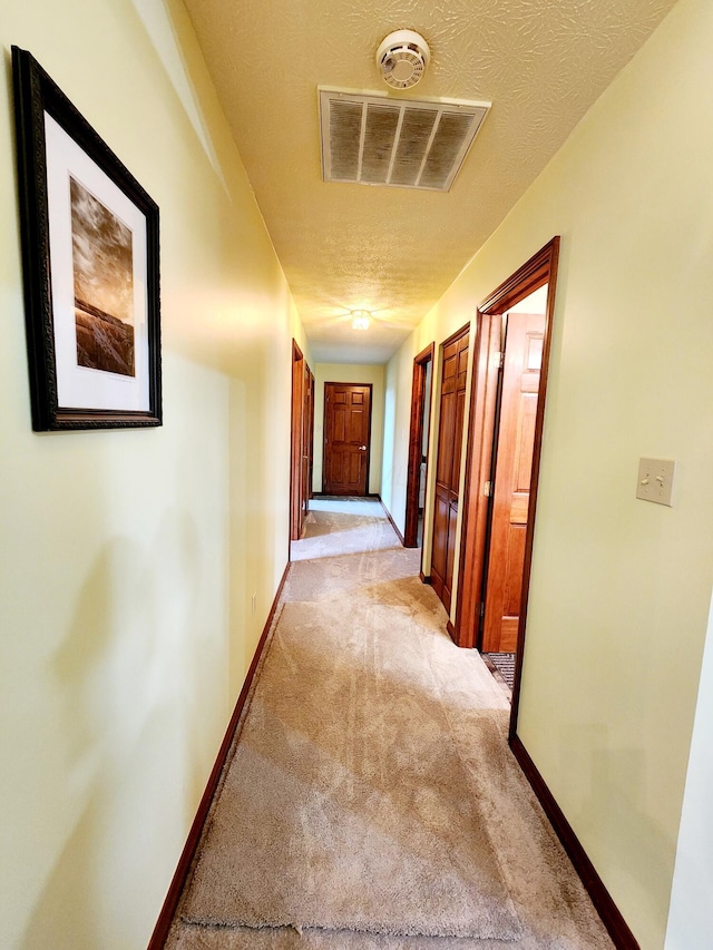 hall with light carpet, baseboards, visible vents, and a textured ceiling