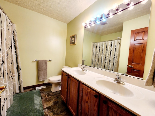 full bath with a textured ceiling, double vanity, a sink, and toilet