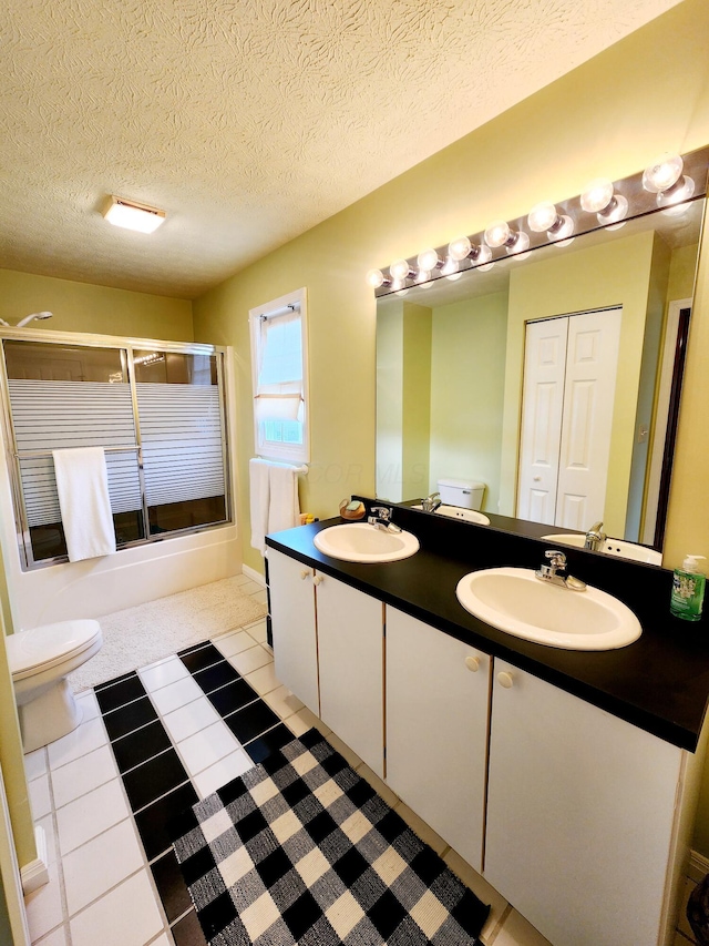 bathroom featuring toilet, double vanity, combined bath / shower with glass door, and a sink