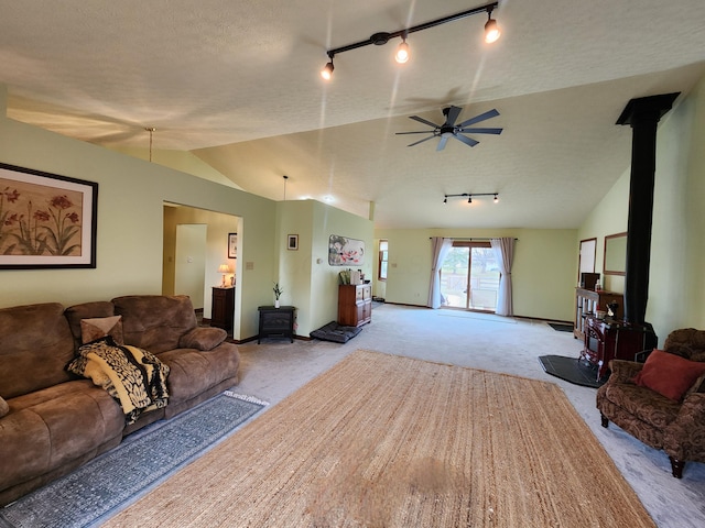 living area featuring carpet floors, a wood stove, vaulted ceiling, and a ceiling fan