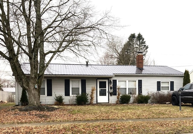 single story home with metal roof, a chimney, and a front yard