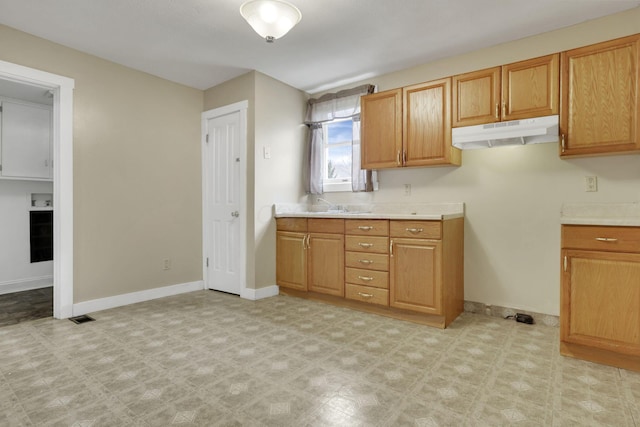 kitchen with under cabinet range hood, baseboards, light countertops, and light floors