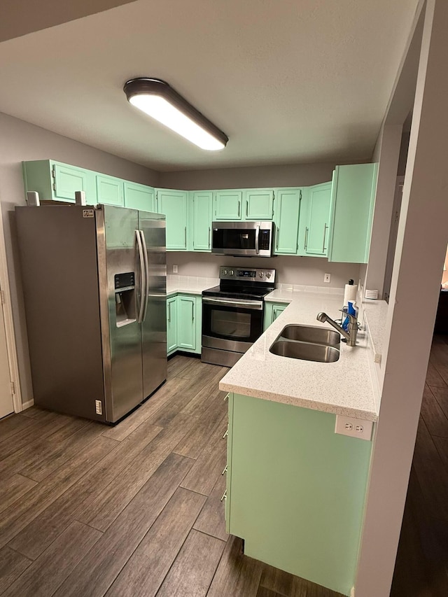 kitchen featuring appliances with stainless steel finishes, dark wood-type flooring, light stone countertops, green cabinets, and a sink