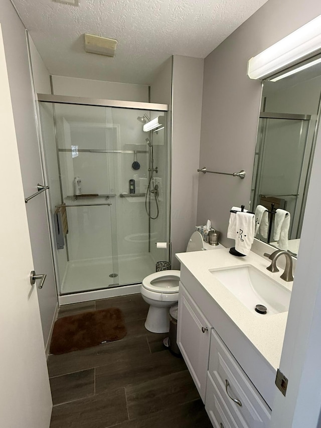 bathroom with toilet, a stall shower, vanity, a textured ceiling, and wood finished floors