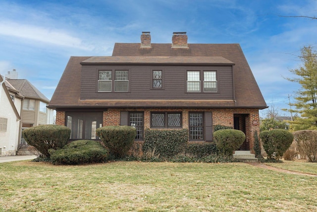 view of front facade with a front yard, brick siding, and a chimney