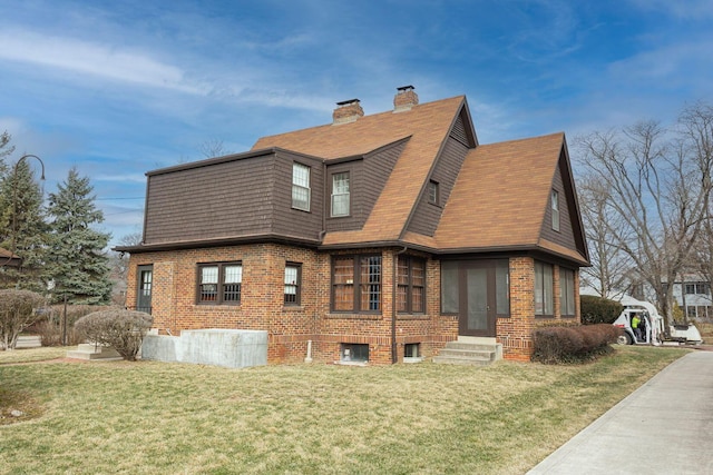 view of side of home with entry steps, a yard, brick siding, and a chimney