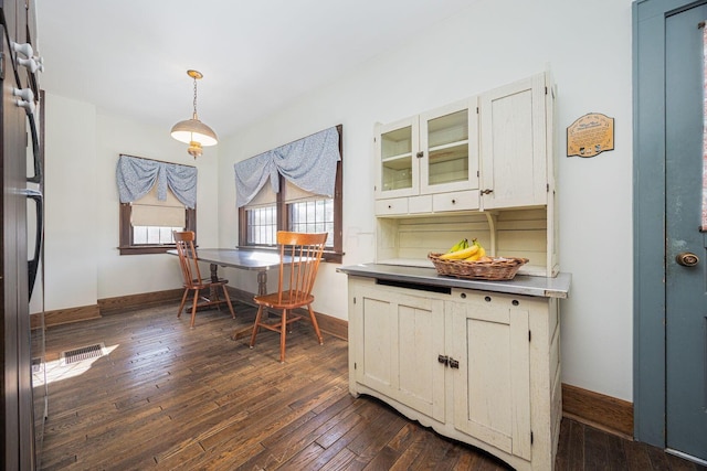 interior space with baseboards, visible vents, dark wood-style floors, glass insert cabinets, and hanging light fixtures