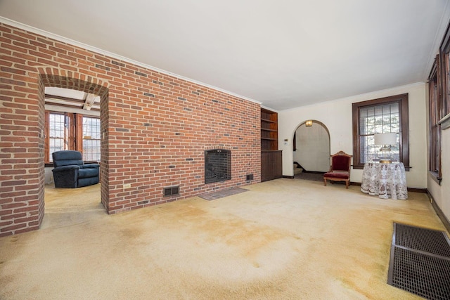 unfurnished living room with visible vents, arched walkways, brick wall, ornamental molding, and carpet