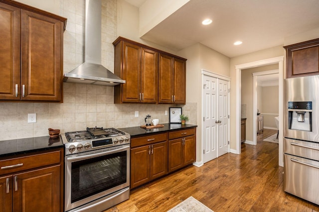 kitchen with baseboards, dark wood finished floors, wall chimney exhaust hood, appliances with stainless steel finishes, and backsplash