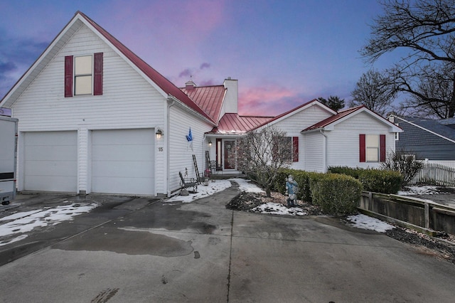 view of front of property featuring driveway, a chimney, metal roof, an attached garage, and a standing seam roof