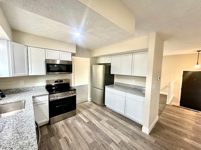 kitchen with stainless steel appliances, light stone counters, light wood-type flooring, and white cabinetry