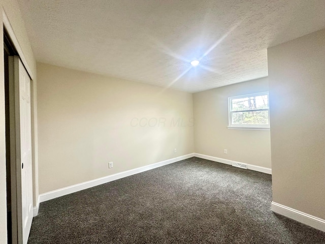 unfurnished bedroom with a textured ceiling, visible vents, baseboards, a closet, and dark carpet