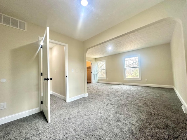 interior space with arched walkways, dark colored carpet, visible vents, a textured ceiling, and baseboards