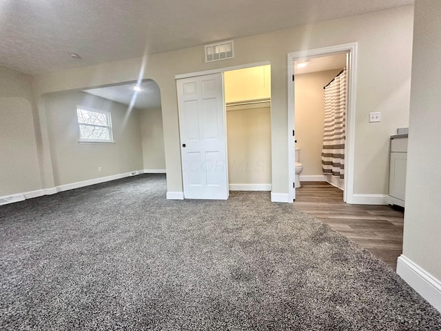 unfurnished bedroom featuring arched walkways, a textured ceiling, connected bathroom, visible vents, and baseboards