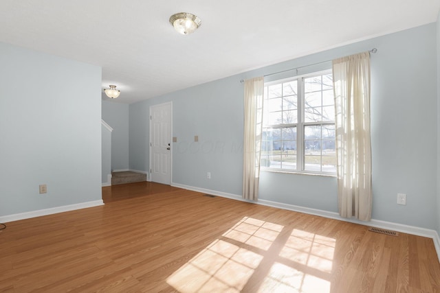 unfurnished room with light wood finished floors, visible vents, and baseboards