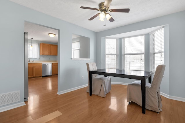 dining room featuring a textured ceiling, light wood finished floors, visible vents, and baseboards