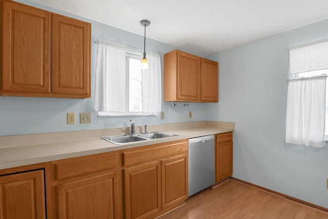 kitchen with light countertops, stainless steel dishwasher, light wood-style floors, pendant lighting, and a sink