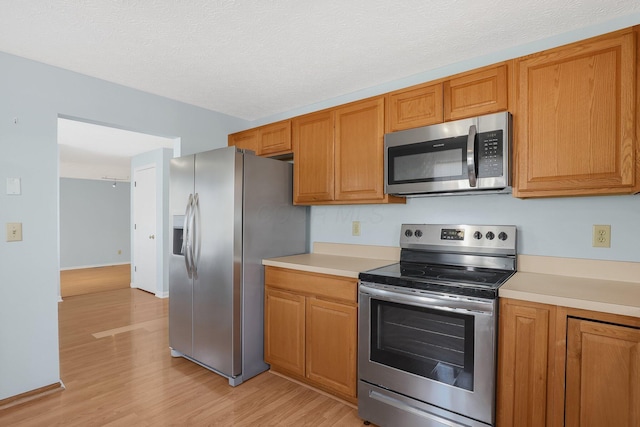 kitchen with a textured ceiling, light wood-style flooring, light countertops, appliances with stainless steel finishes, and brown cabinets