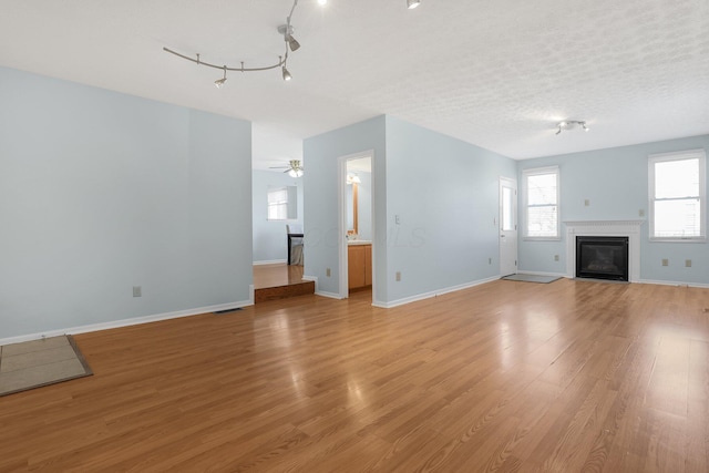 unfurnished living room with light wood finished floors, baseboards, a textured ceiling, and a glass covered fireplace