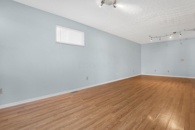 unfurnished room featuring rail lighting, visible vents, light wood-style floors, a textured ceiling, and baseboards