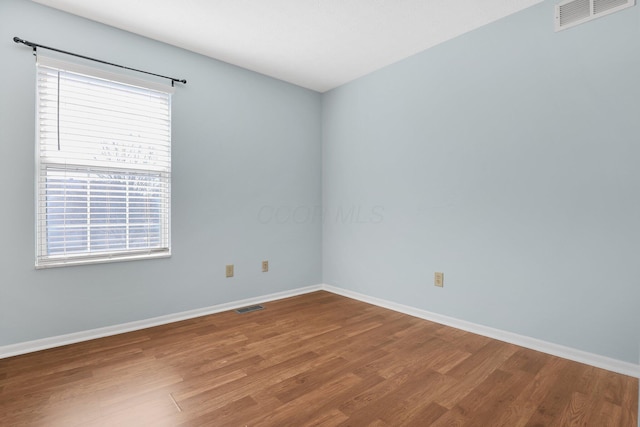 spare room with wood finished floors, visible vents, and baseboards