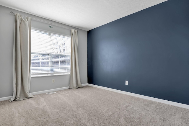 spare room with carpet floors, visible vents, baseboards, and a textured ceiling