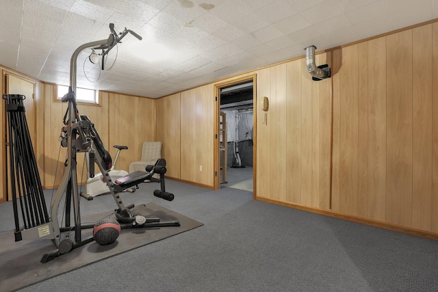 exercise room with baseboards, light colored carpet, and wooden walls