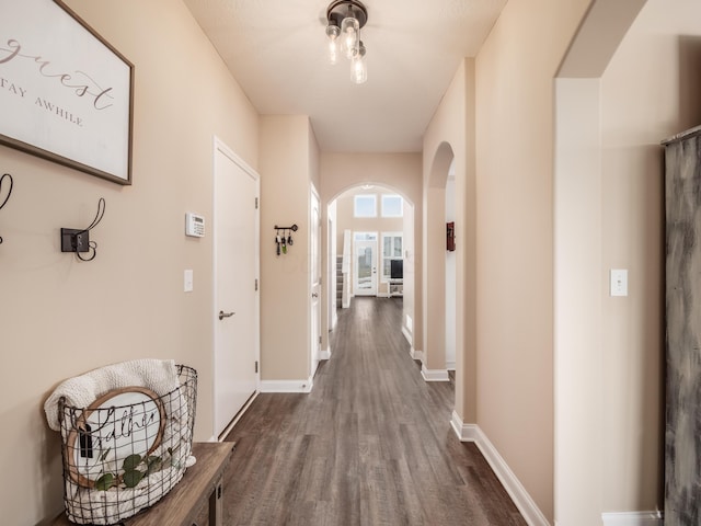 hall with baseboards, arched walkways, and wood finished floors