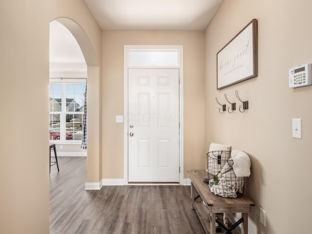 entryway with arched walkways, wood finished floors, and baseboards