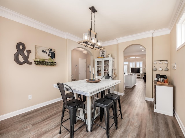 dining room with arched walkways, dark wood-type flooring, and ornamental molding