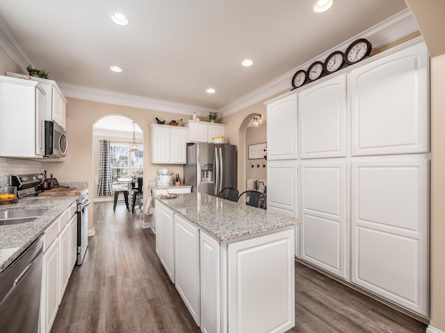 kitchen with arched walkways, stainless steel appliances, a kitchen island, and white cabinetry