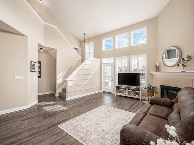 living area with a high ceiling, dark wood-style flooring, a fireplace, baseboards, and stairway