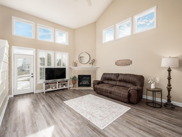 living room featuring a high ceiling, a fireplace, wood finished floors, and baseboards