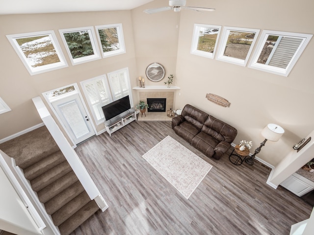 living room featuring a tile fireplace, wood finished floors, a towering ceiling, baseboards, and stairway