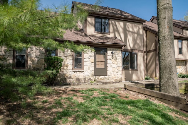 rear view of house with roof with shingles, stucco siding, and stone siding