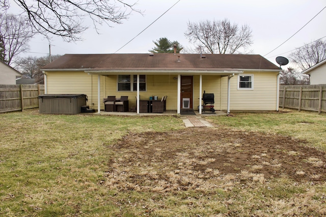 back of house with a yard, a patio area, a fenced backyard, and a hot tub