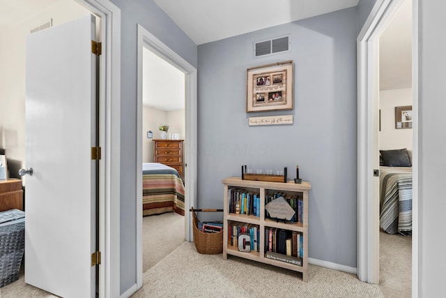 hall with baseboards, visible vents, and light colored carpet