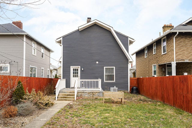 rear view of property featuring a chimney, cooling unit, a fenced backyard, and a gambrel roof